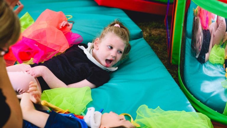 a child at chestnut lying on a green mat surrounded by colourful fabrics. She is looking into a mirror