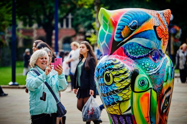 Image of a large colourful owl sculpture with a woman infront taking a photograph.