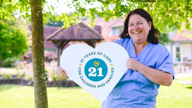 Image of a nurse holding a love heart with our 21 anniversary logo on it - reading: 21 years of care for children and families