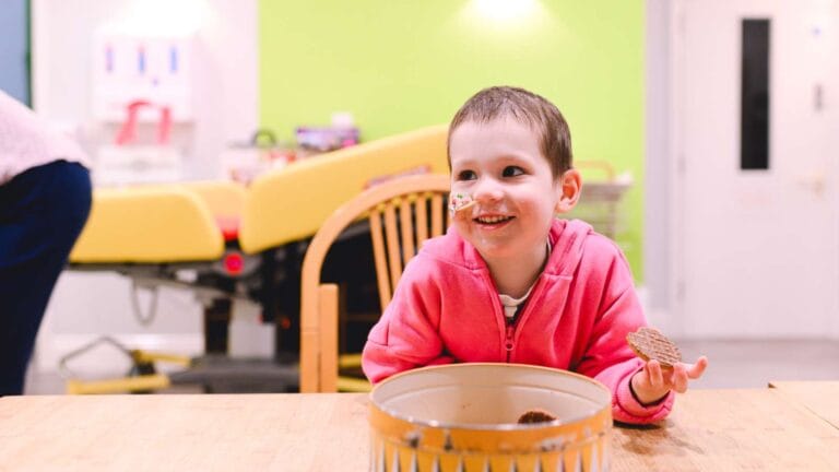 Child with a tube out of their nose, eating a chocolate biscuit and smiling.