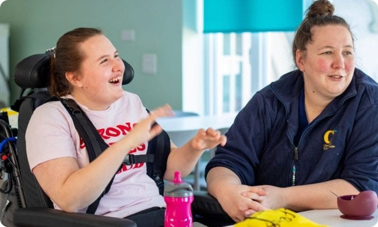 A nurse sits with a young person smiling at a table.