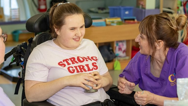 A young person sits in the crafts area at Chestnut Tree House while an activities team member uses Makaton to communicate with them