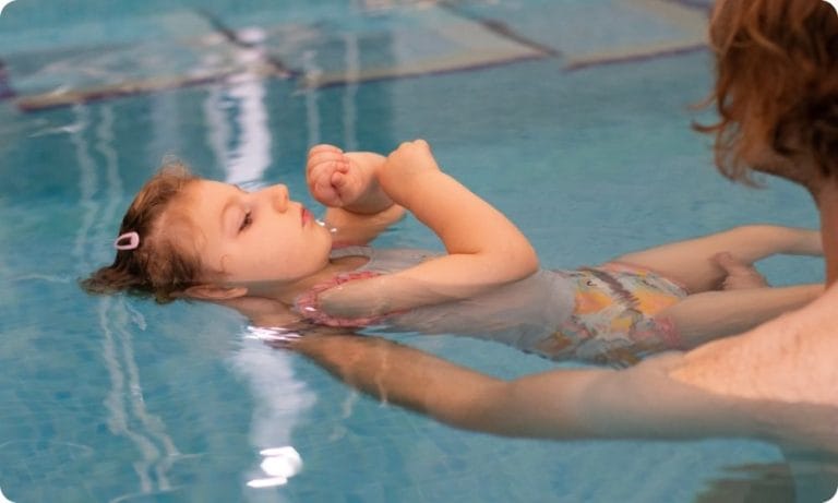 A little girl floats in the hydrotherapy pool at Chestnut Tree House, helped by her dad