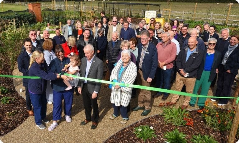 A crowd stands in the kitchen garden as one of the Chestnut children helps cut the ribbon