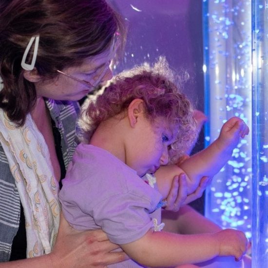 A little girl looks at a bubble tower with her mum in the sensory room at Chestnut Tree House