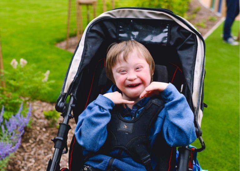 child in a buggy in the Chestnut Tree House garden, smiling at the camera