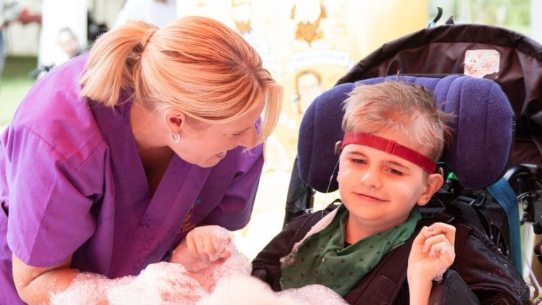 a member of the care team with a boy in a wheelchair, they are playing with lots of bubbles