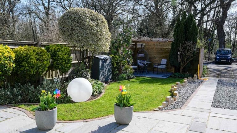A sunny garden with flower pots, a path and a globe water feature.