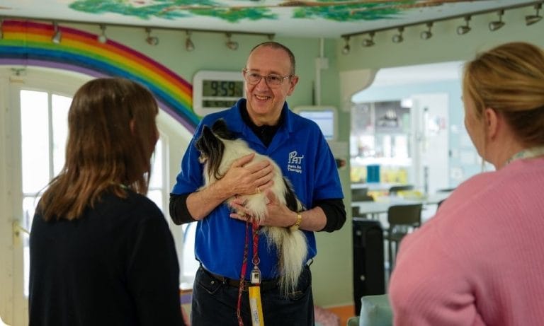 A man stands holding a small dog and smiling at a woman