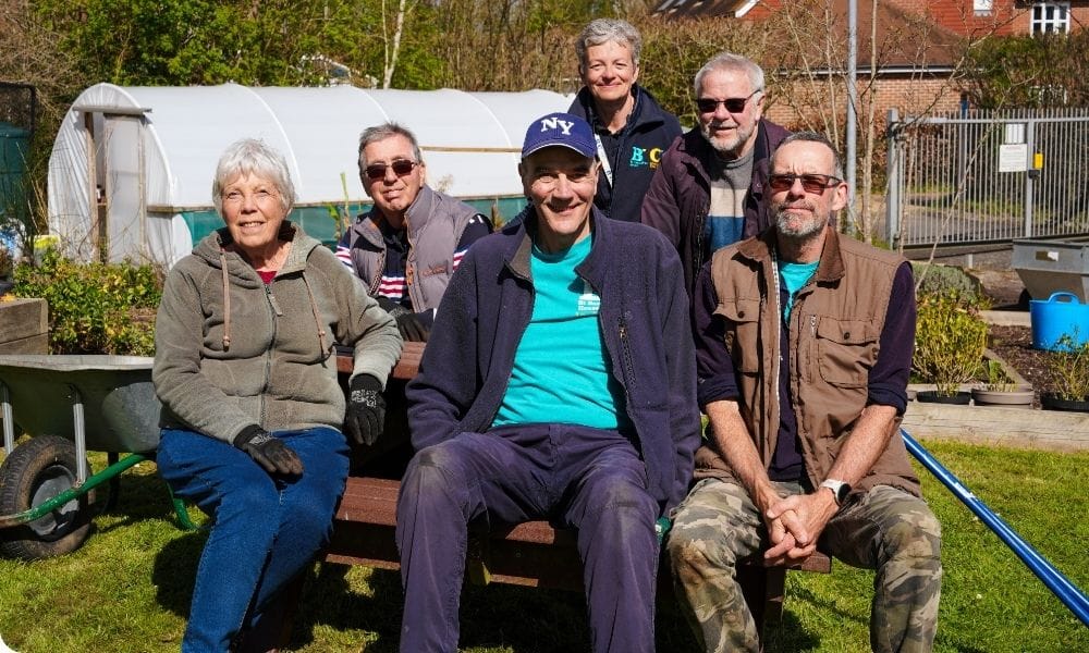A group of people sits in a sunny garden smiling at the camera.