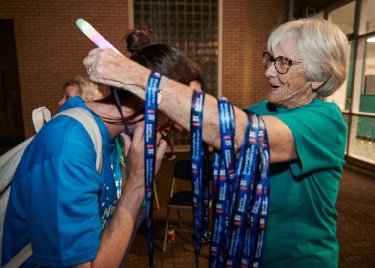 a volunteer at Night to Remember with an armful of medals, presenting a walker with their medal